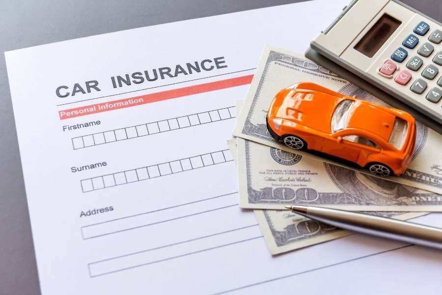 Un formulaire "ASSURANCE AUTO" vierge avec un stylo, une calculatrice et une voiture miniature orange posée sur des billets de banque.