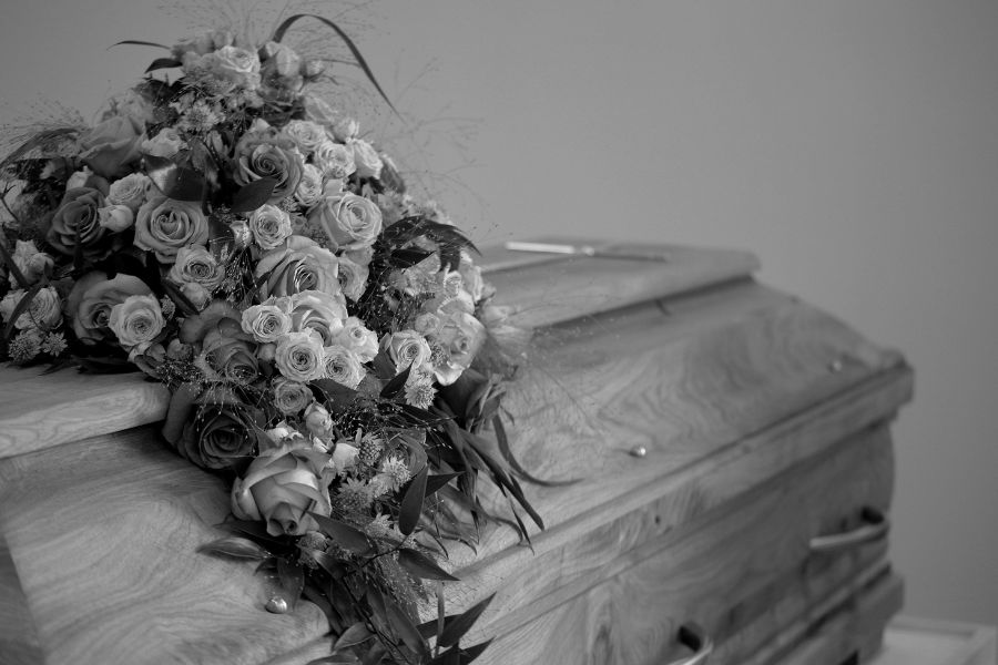 Un cercueil en bois orné d'un bouquet de fleurs en noir et blanc, symbolisant le deuil et la prévoyance d'une assurance décès.